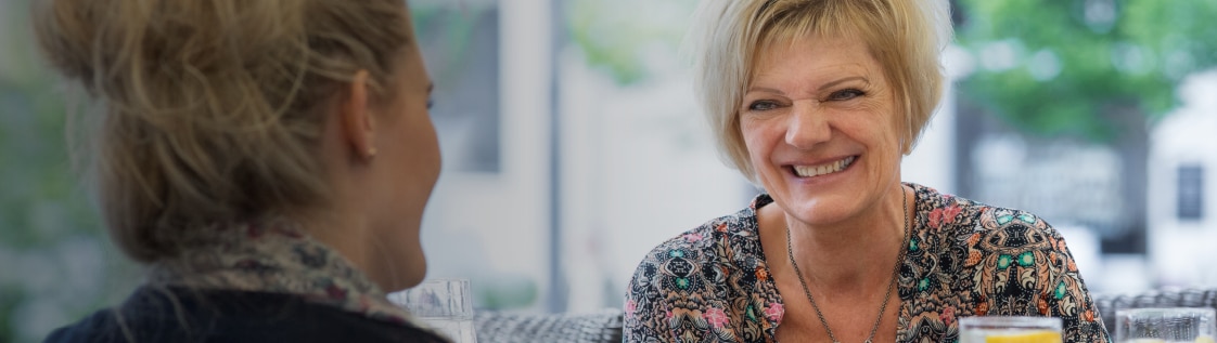 Margit, Anwenderin von SenSura Mio, lachend mit einer Freundin beim Mittagessen. 