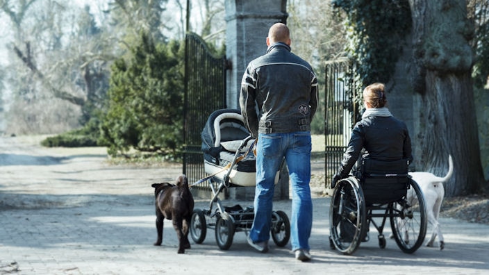 Mann mit Kinderwagen und Frau im Rollstuhl gehen mit Hunden spazieren