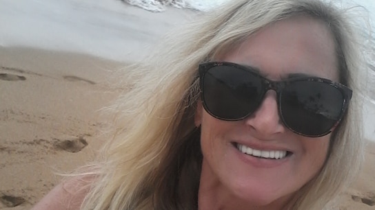 Frau mit Sonnenbrille am Strand lacht in die Kamera