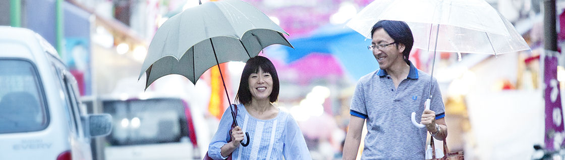 Pärchen geht Hand in Hand lachend mit Regenschirmen durch die Stadt